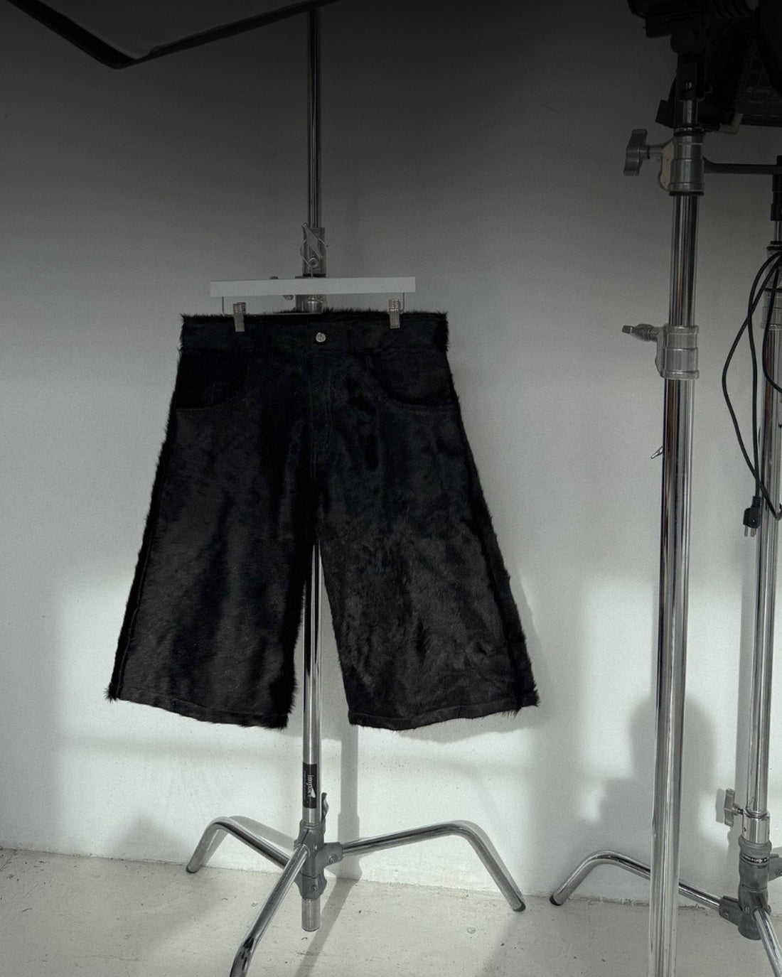 Black shorts on a hanger clipped to a light stand, lit by window light in a white studio